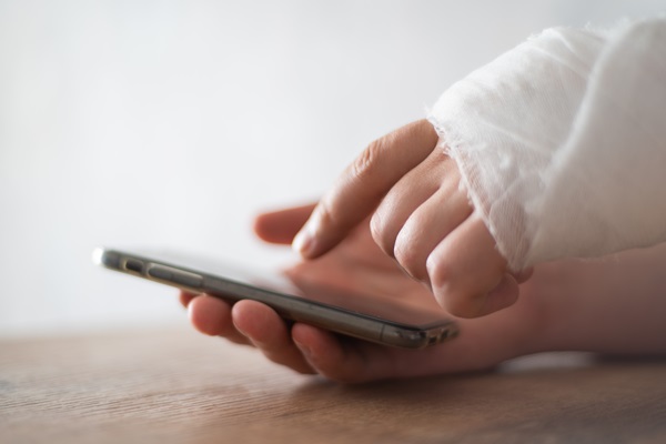 Fracture hand in bandage getting ready to call a workers' comp lawyer on the phone.